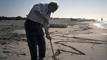 An elderly gentleman, painting in the sand with his barge